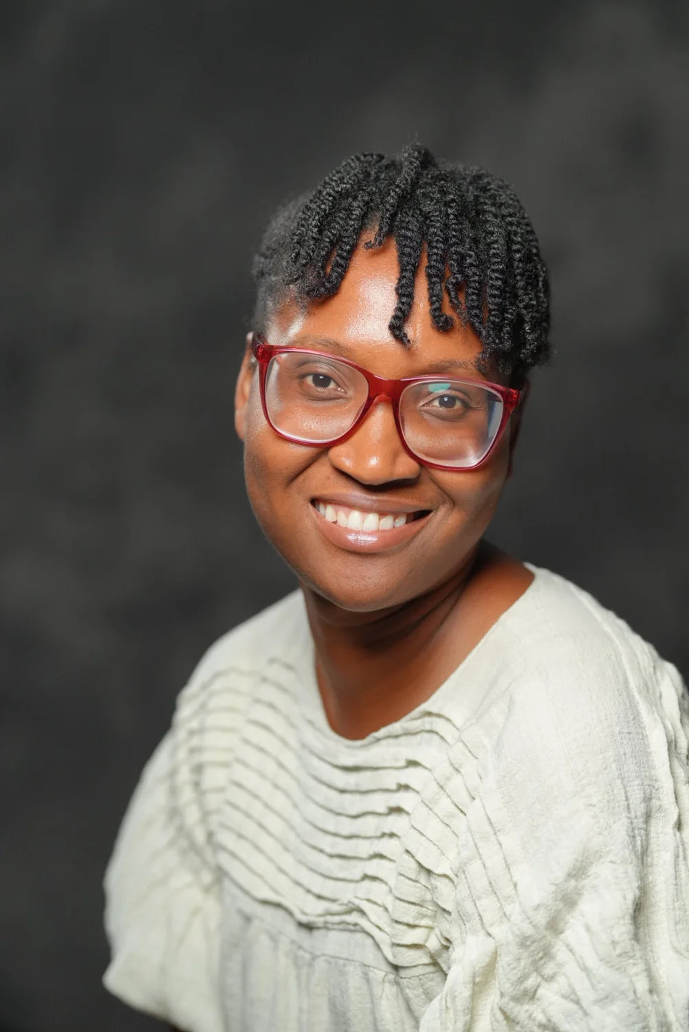 Dr. Shonoi Ming smiling in red glasses and a cream top