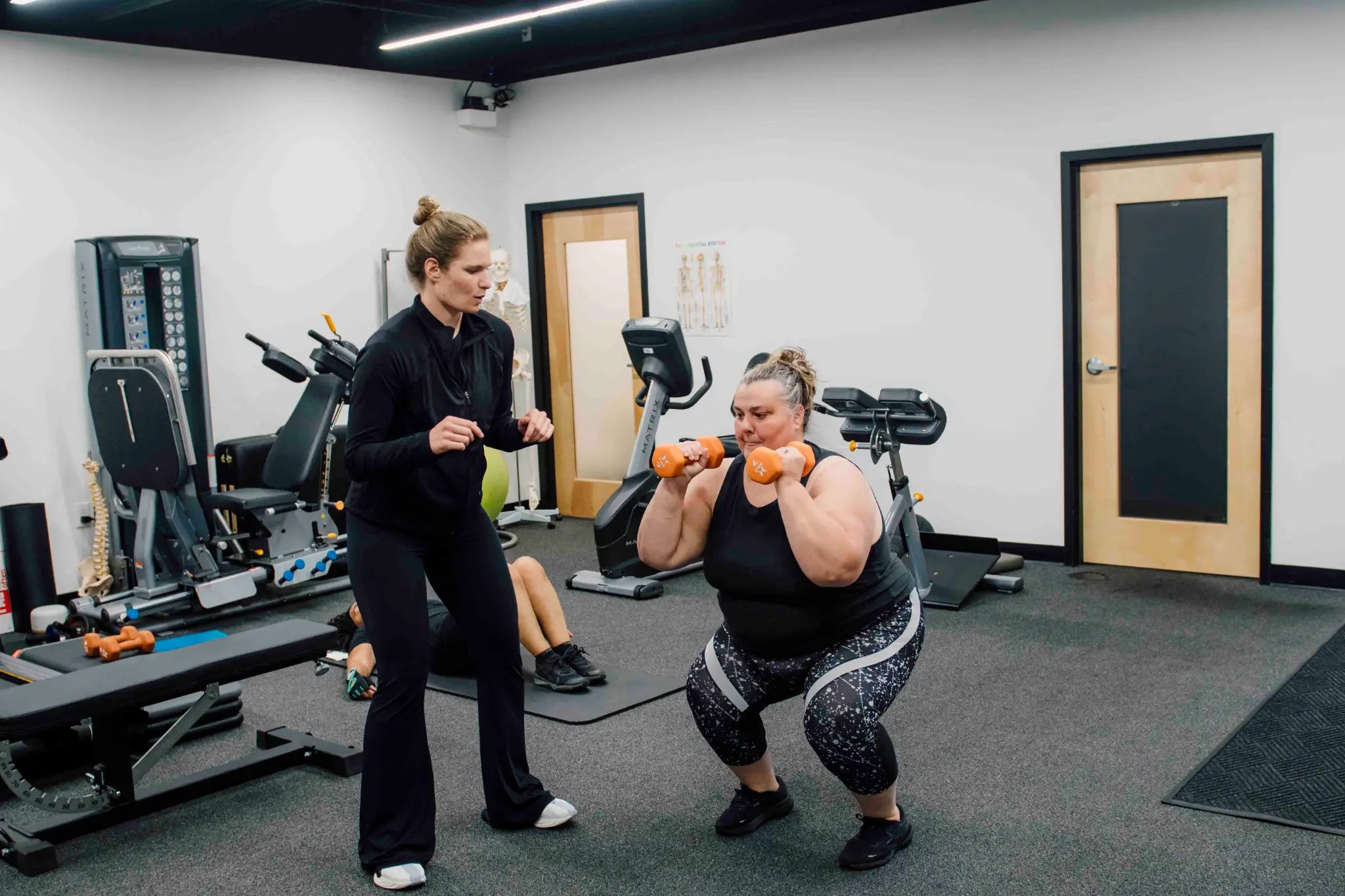 An ANTIOX coach supporting a person exercising with orange dumbbells in the studio